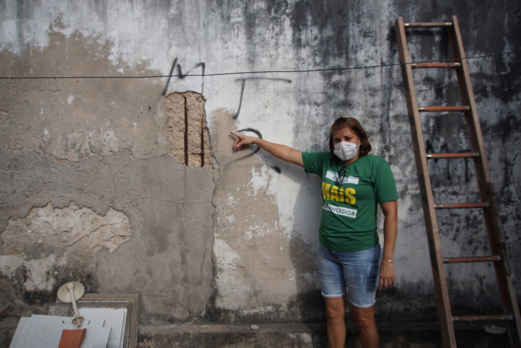 Darcilene Moura ao lado de um dos danos causados pelo incêndio, esse muro fica no quintal da sua casa, próximo ao muro da loja. Foto: Kethlen Mata / Atual7